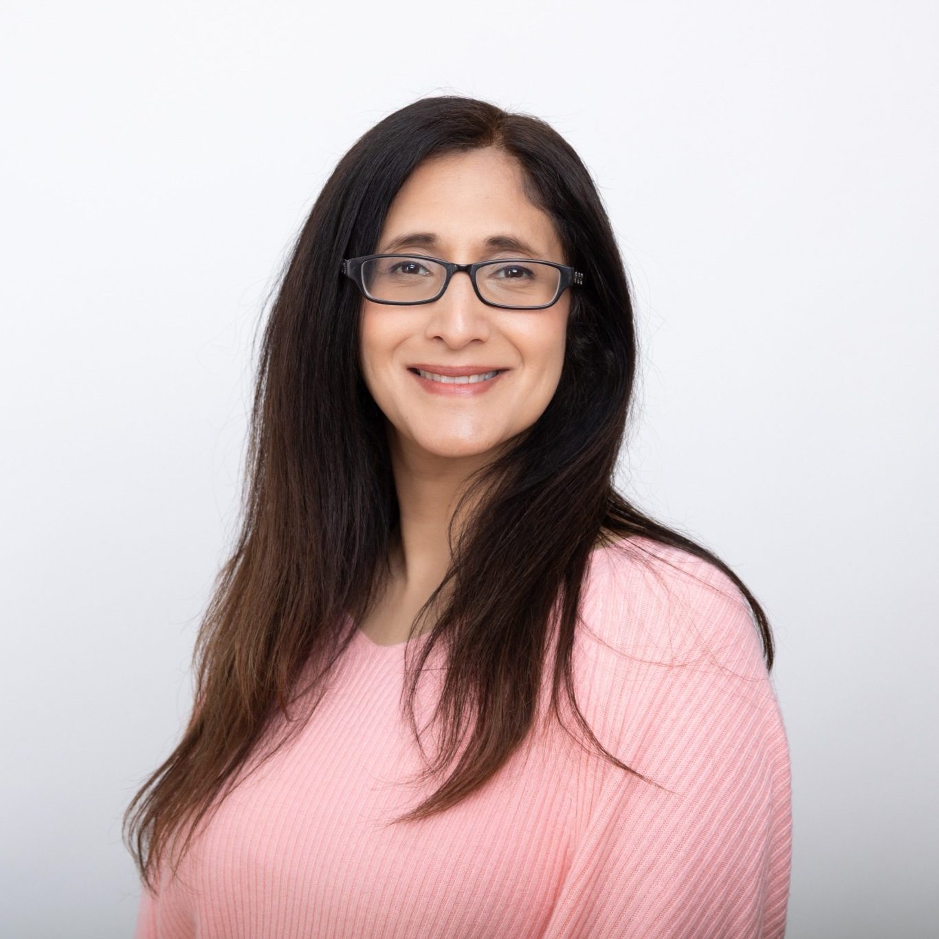 A woman with long, dark hair smiles against a pink background.